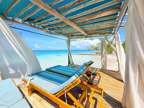 A wooden deck with two lounge chairs, a covered area with a blue mesh roof, and a view of the ocean. - Hotel Isla Palma (Isla Palma)