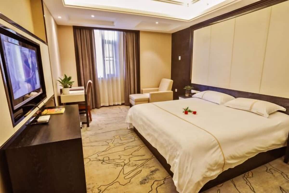 A hotel room with a bed, a desk with a TV, a chair, and a window with curtains.