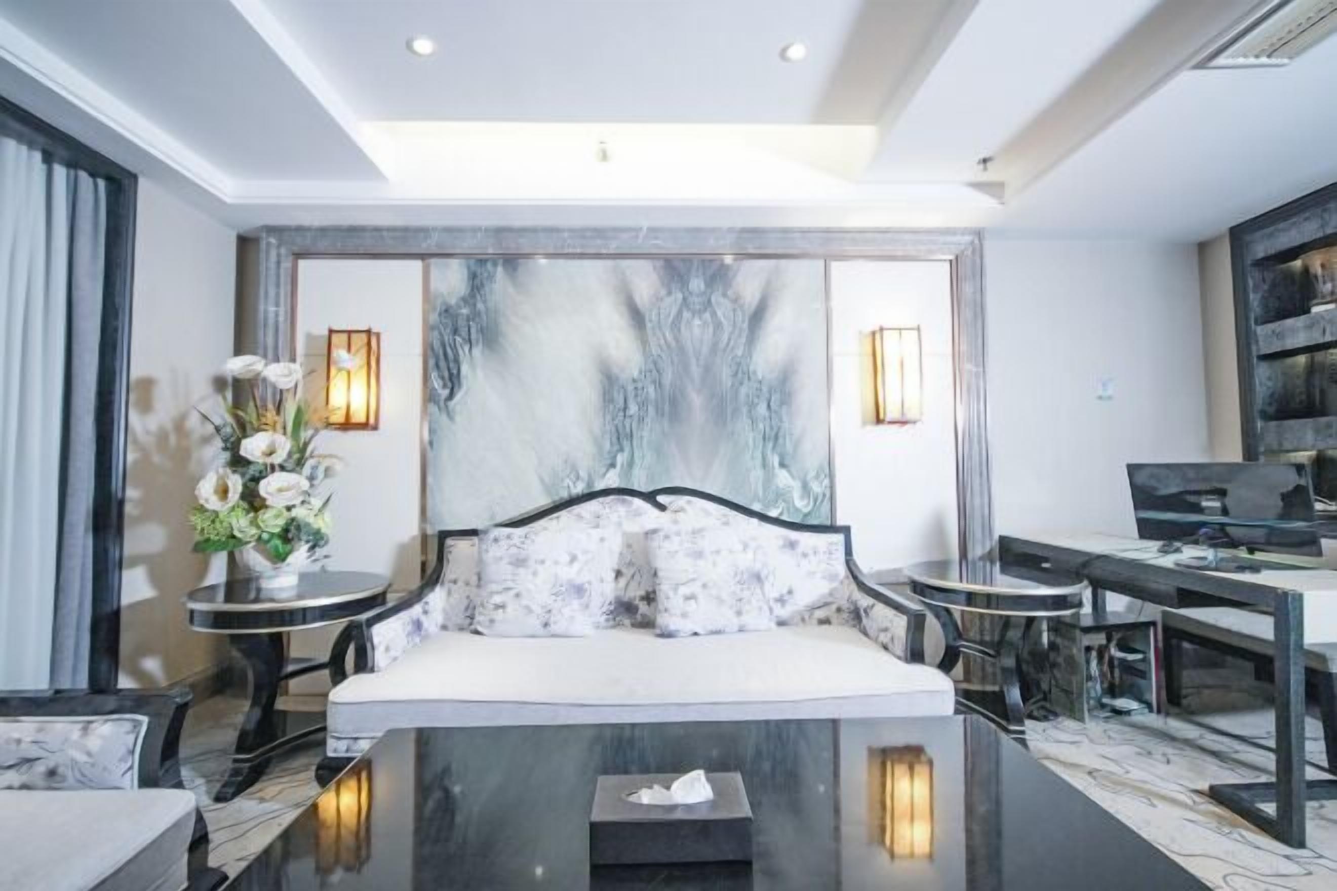 Habitación de hotel moderna con una pared de acento de mármol, una cama sofá, una mesa de comedor y una mesita auxiliar con un jarrón de flores.