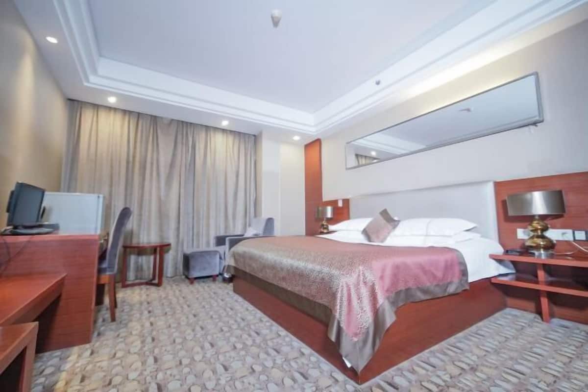 A hotel room with a large bed, a desk with a computer, a chair, a small table, and a mirror on the wall.