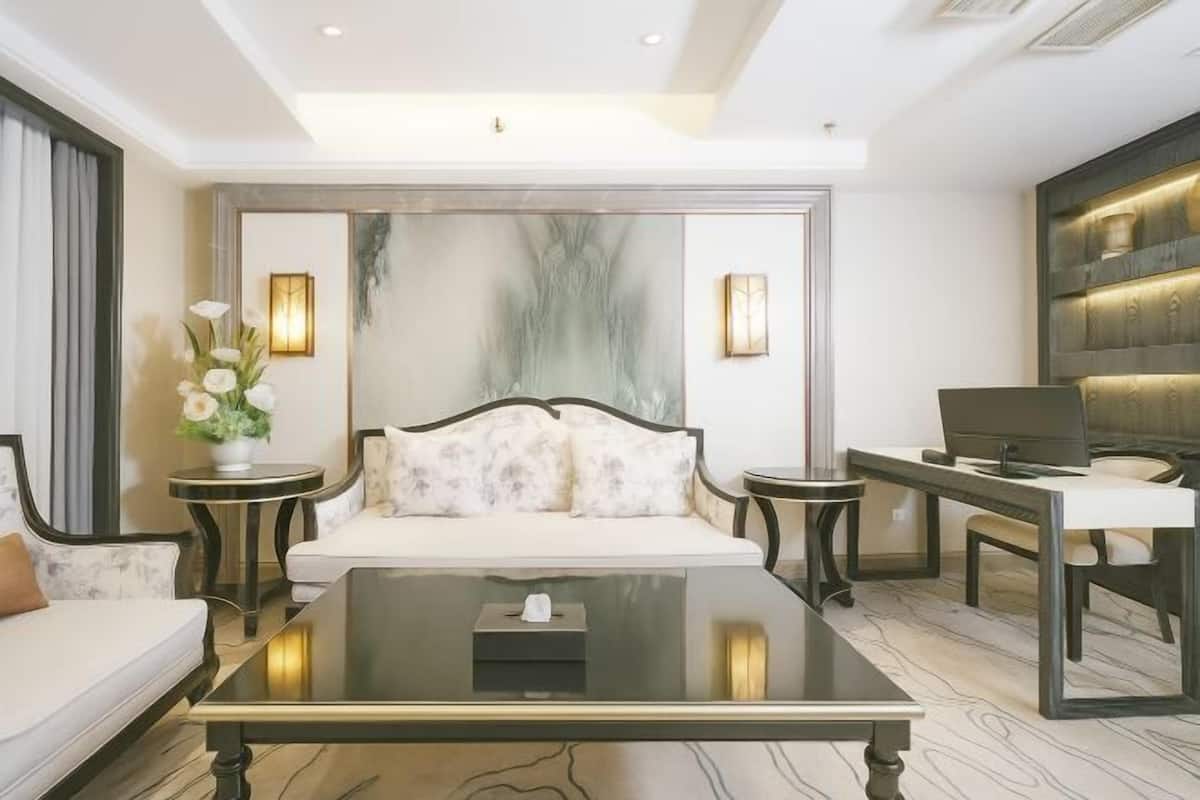A modern hotel room with a bed, a sofa, a coffee table, a desk, and a wall-mounted TV.