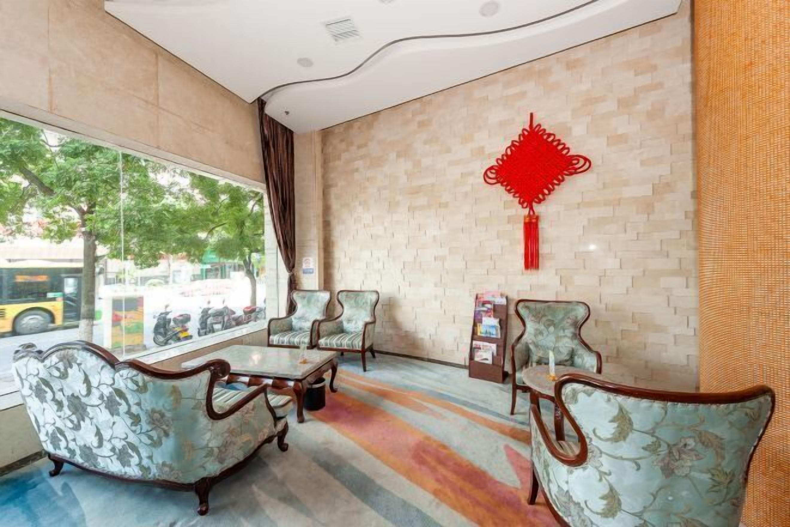 A lobby with a large window, patterned chairs, a small table, and a decorative red wall hanging.