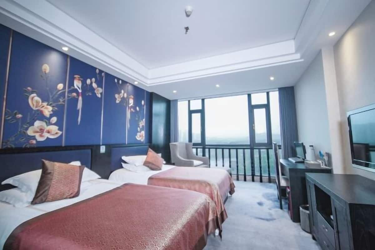A hotel room with two beds, a desk, a chair, a TV, and a balcony with a view.
