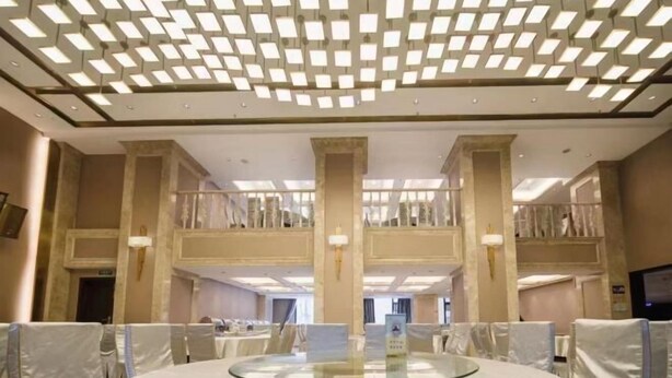 A hotel lobby with a central round table, high ceilings with patterned lighting, and a mezzanine level. - Victoria Royal Hotel (Shangrao)