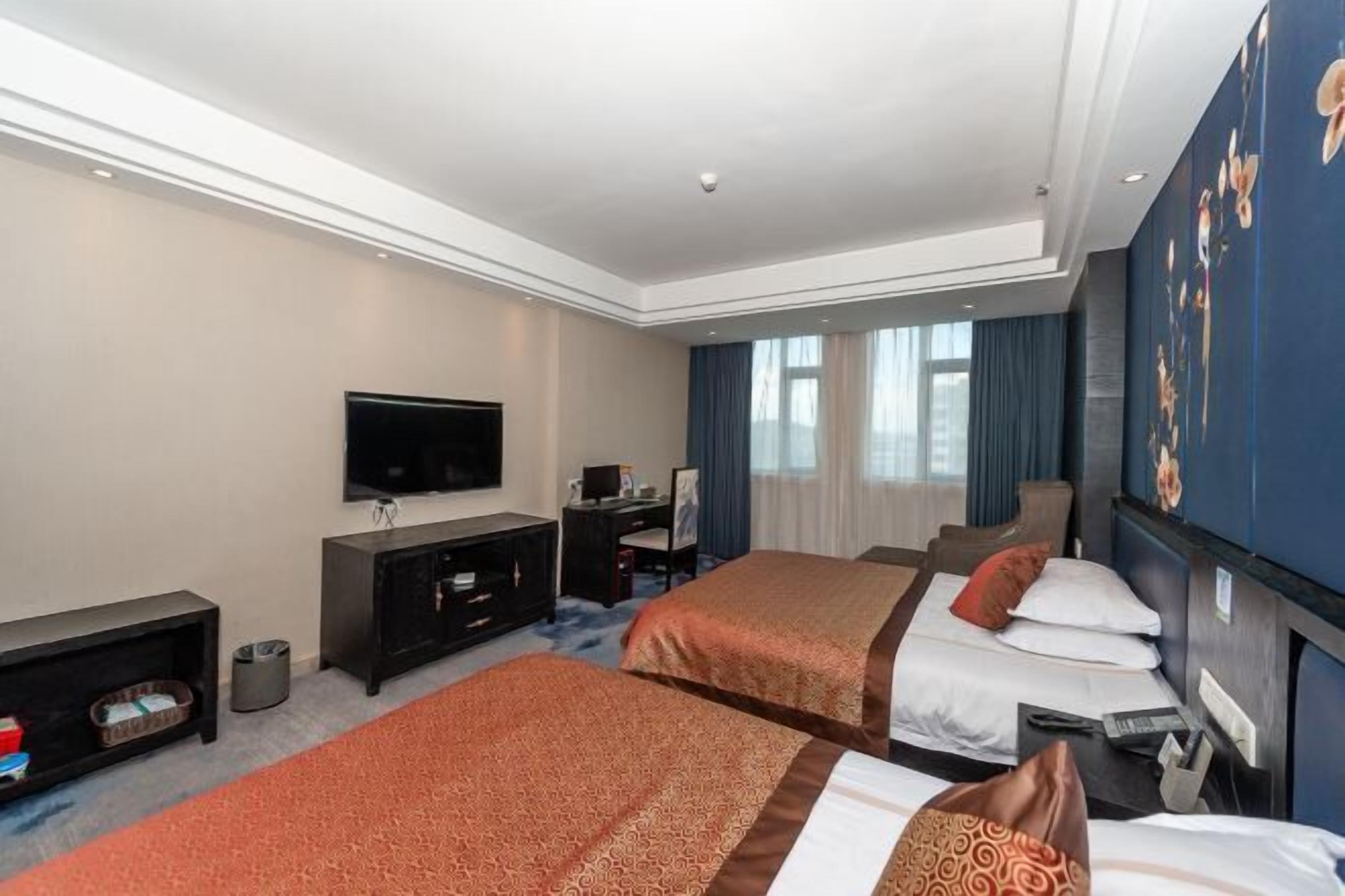 Une chambre d’hôtel avec deux lits, une télévision, un bureau et une grande fenêtre avec des rideaux.