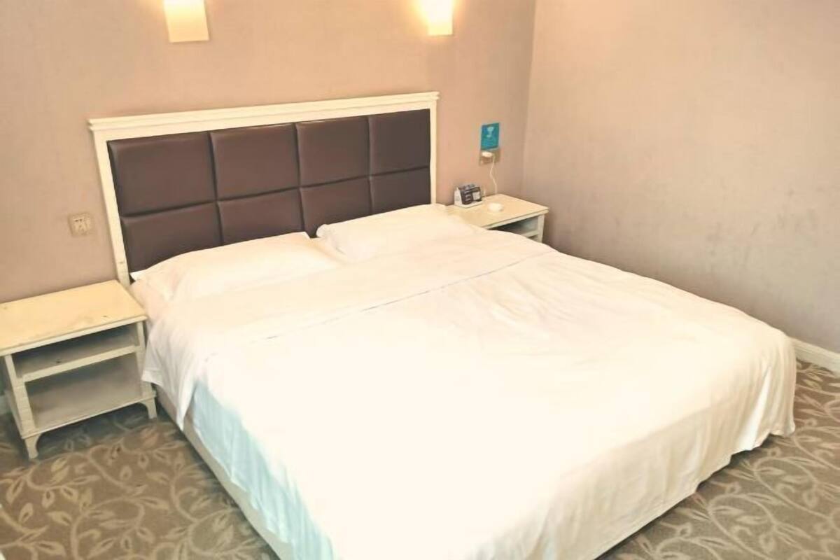 Un lit bien fait, avec une tête de lit, une table de chevet et un luminaire fixé au mur.