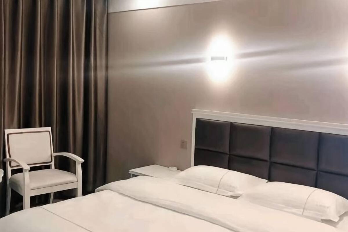 Une chambre d’hôtel avec un lit, une chaise, une table de chevet et une lampe fixée au mur.
