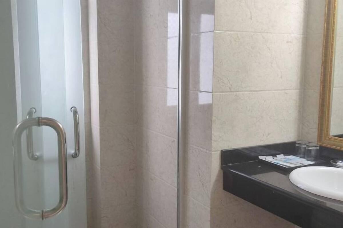 Une salle de bain avec une porte en verre, un comptoir noir, un lavabo blanc et un miroir avec un cadre doré.