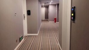 A hotel hallway with striped carpet, a door with a keypad, and a trash bin. - Hongyang Hotel (Chongqing)