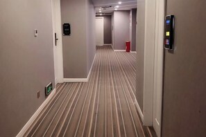 Un pasillo de hotel con alfombra a rayas, una puerta con teclado numérico y un cesto de basura.