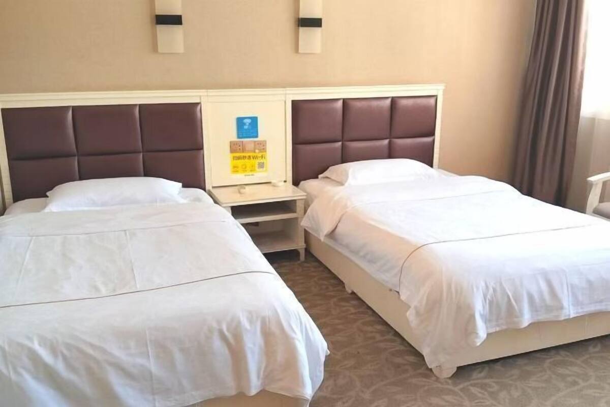 Une chambre d’hôtel avec deux lits, une table de chevet et un luminaire fixé au mur.