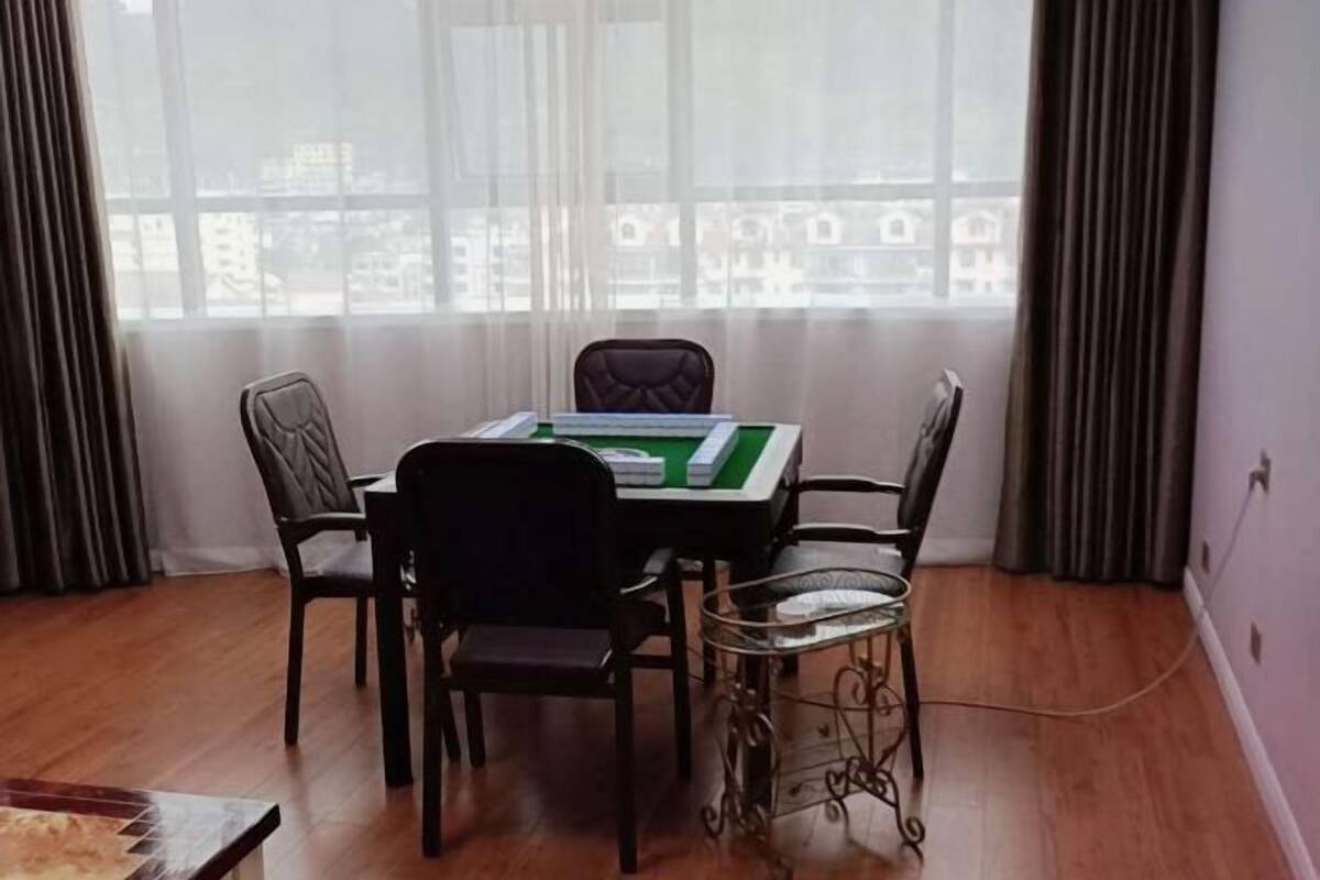 Une pièce avec une table dressée pour deux personnes, une chaise, une table basse en verre et une vue par une fenêtre avec des rideaux.