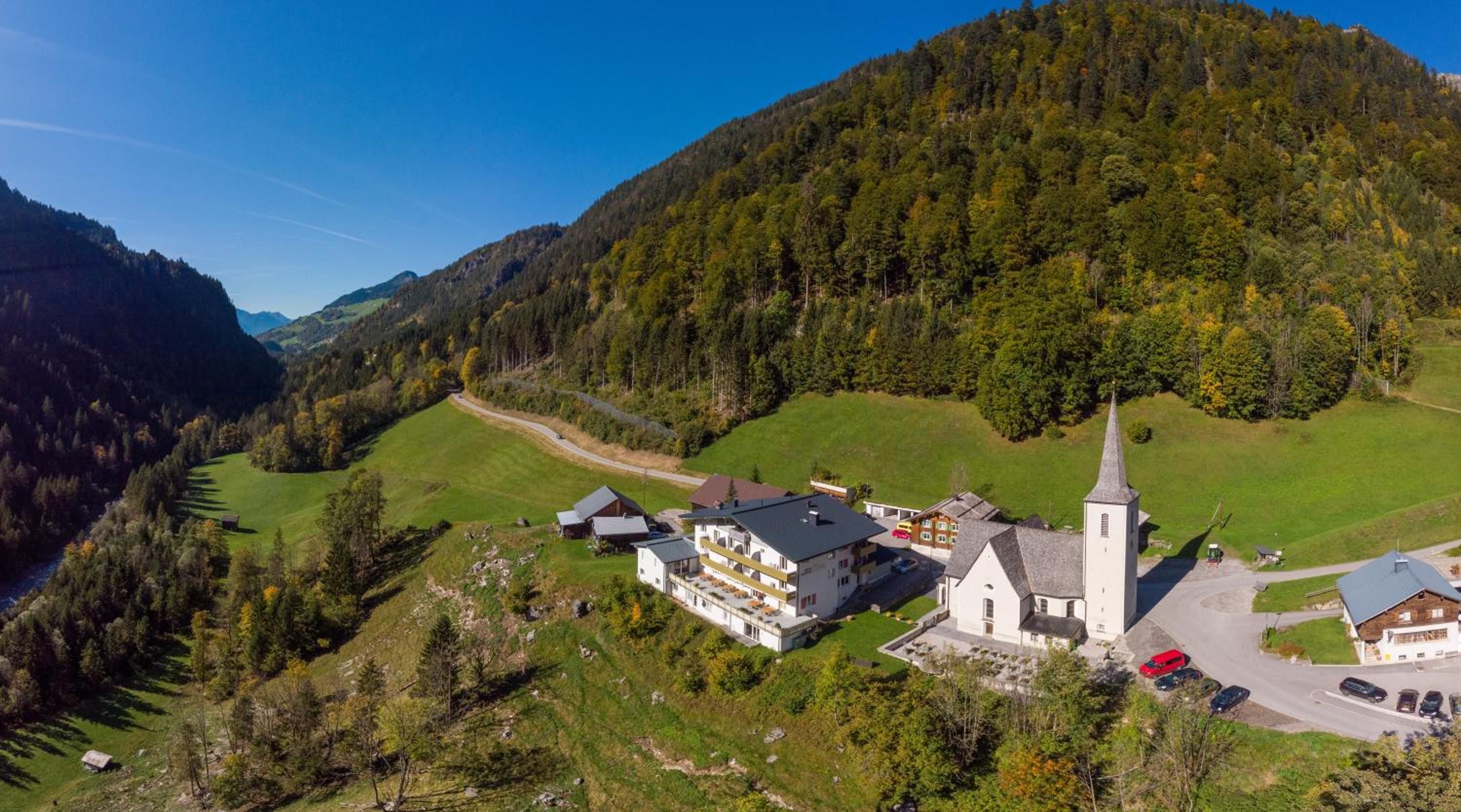 Un pueblo montañoso con una iglesia, edificios residenciales y una carretera serpenteando por el valle.