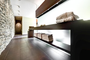 A modern bathroom with a stone wall, a wooden shelf with towels, and a tiled floor.