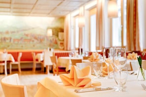 Ein Restaurantambiente mit gedeckten Tischen, inklusive ordentlich gefalteter Servietten und klarem Glasgeschirr.