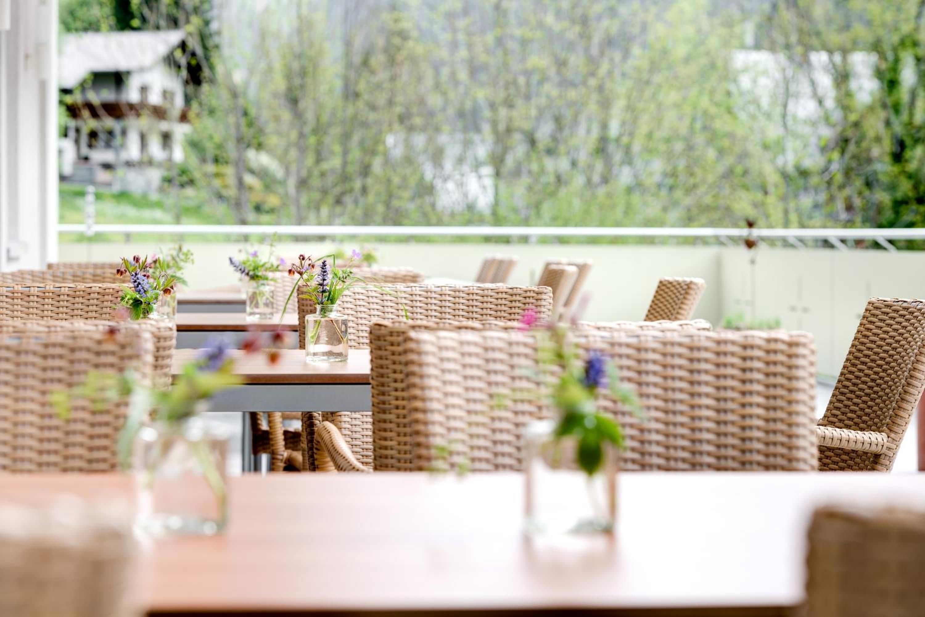 Un restaurante con mobiliario de mimbre y mesas de vidrio, que ofrece terraza con vistas a zonas verdes.