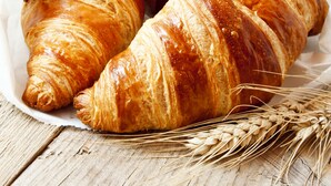 Drei Croissants auf einer Holztischplatte, mit Weizenhalmen.