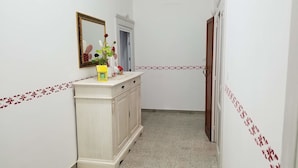 Ein schmaler Flur mit weißer Wand, einem cremefarbenen Schrank, einem Spiegel und einer Tür.