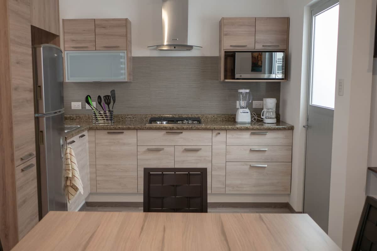 A modern kitchen with wooden cabinets, a stainless steel refrigerator, a microwave, and a coffee maker.