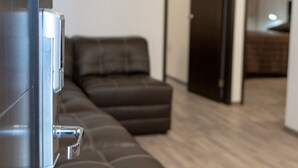 Un salón moderno con un sofá de cuero marrón, suelo de madera y una puerta que da a otra habitación.