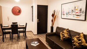 Un salon avec un canapé en cuir marron, une table basse, une table à manger avec des chaises, un élément de décoration murale circulaire rouge et un tableau encadré représentant des voiliers.