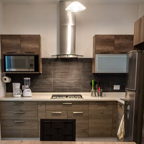 Una cocina moderna con gabinetes de madera, campana extractora de acero inoxidable, microondas, refrigerador y cafetera.