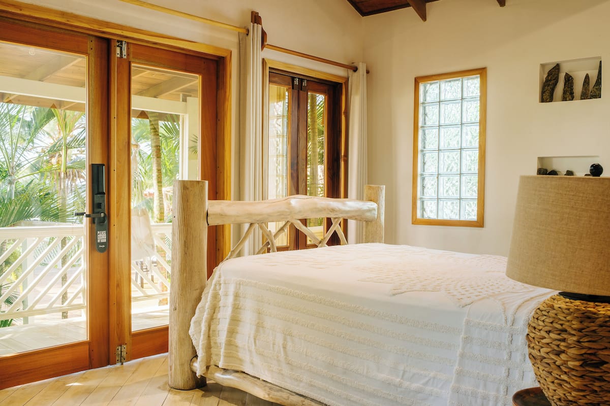 A bedroom with a bed, a wooden door, a window, and a lamp.