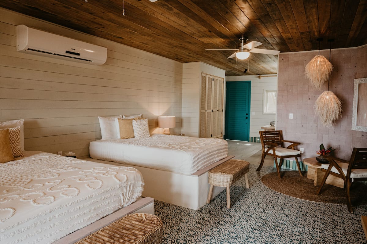 A room with two beds, a ceiling fan, a desk with chairs, and a small table with a plant.