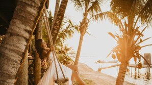 Una persona descansando en una hamaca entre palmeras, con vista a una playa.