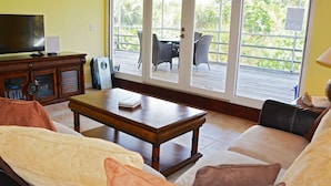 A living room with a sofa, coffee table, and a television. There is a sliding glass door leading to an outdoor patio with chairs and a table. - The Little Oasis Beach House (Captiva)