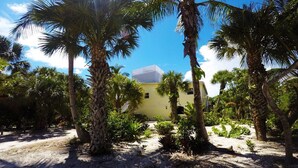 A yellow building surrounded by palm trees and tropical vegetation. - The Little Oasis Beach House (Captiva)