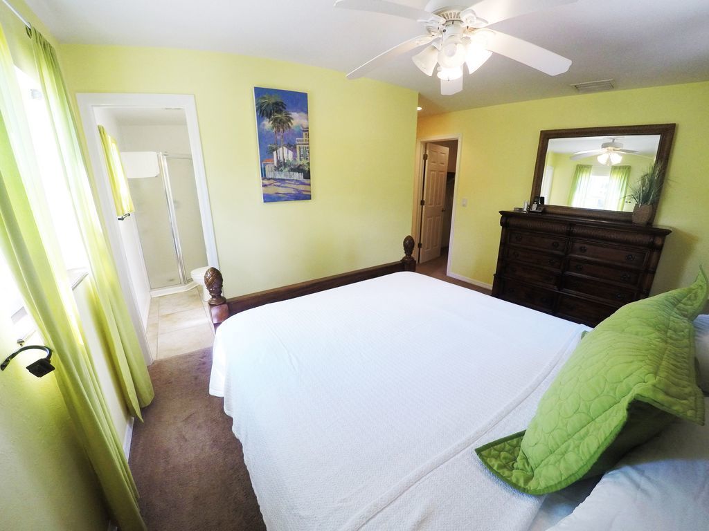 Un dormitorio con cama, ventilador de techo, cómoda y puerta que da a un baño.