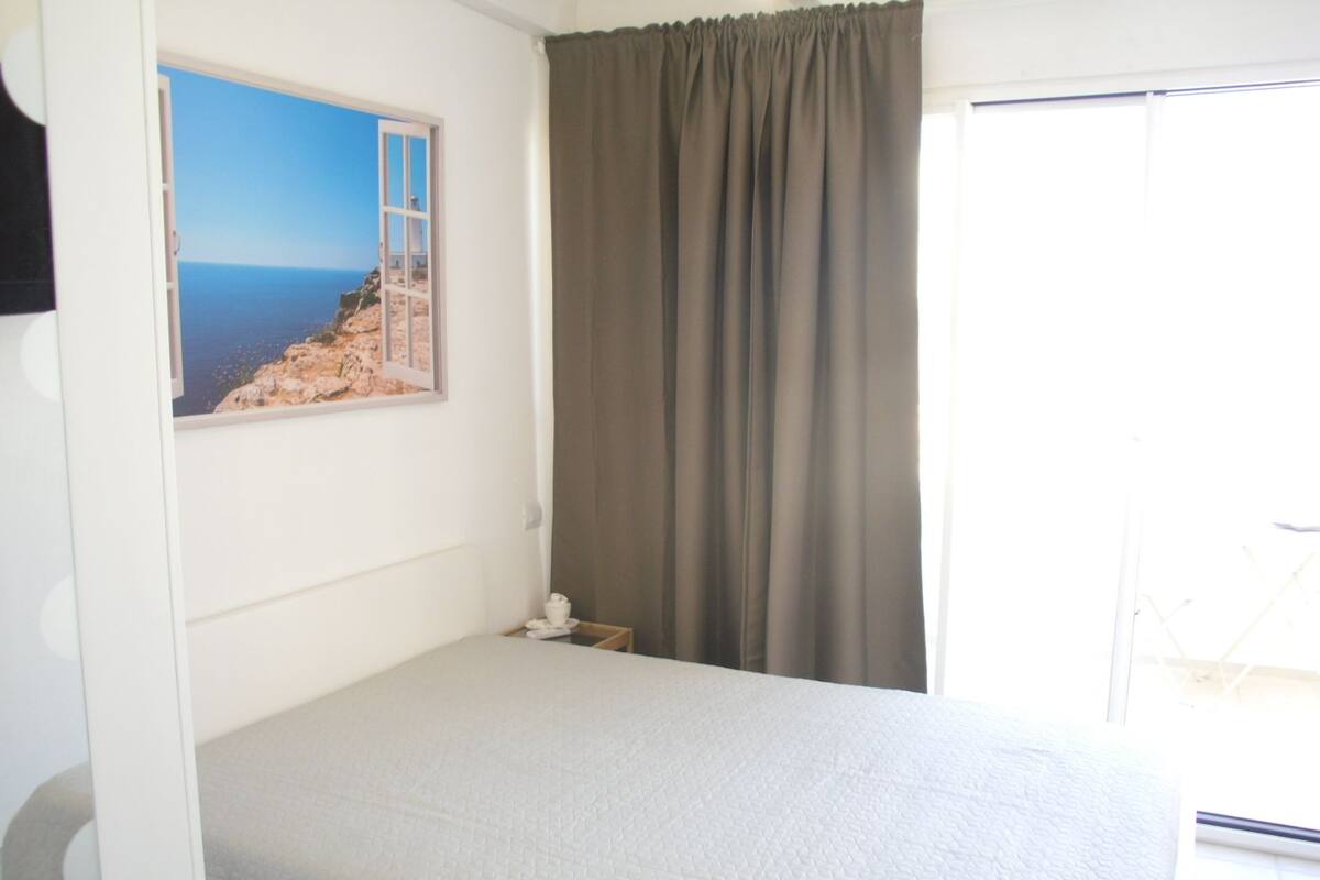 Un dormitorio con cama, ventana con vista al mar y cortina.