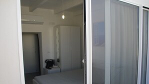 A bedroom with a bed, a nightstand, a mirror, and a sliding glass door leading to a balcony. - Romì (Polignano a Mare)