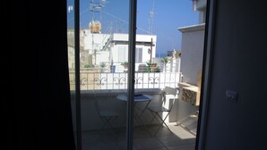 A balcony with a table and chairs, a small garden area with potted plants, and a view of the sea and other buildings. - Romì (Polignano a Mare)