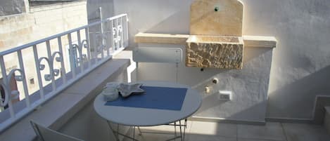 A balcony with a white table and chair, a small grill, and a stone shelf.