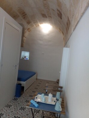 A small, cozy room with a sloped ceiling, a bed, a table with a tray of cups, and a small television on the wall. - Romì (Polignano a Mare)