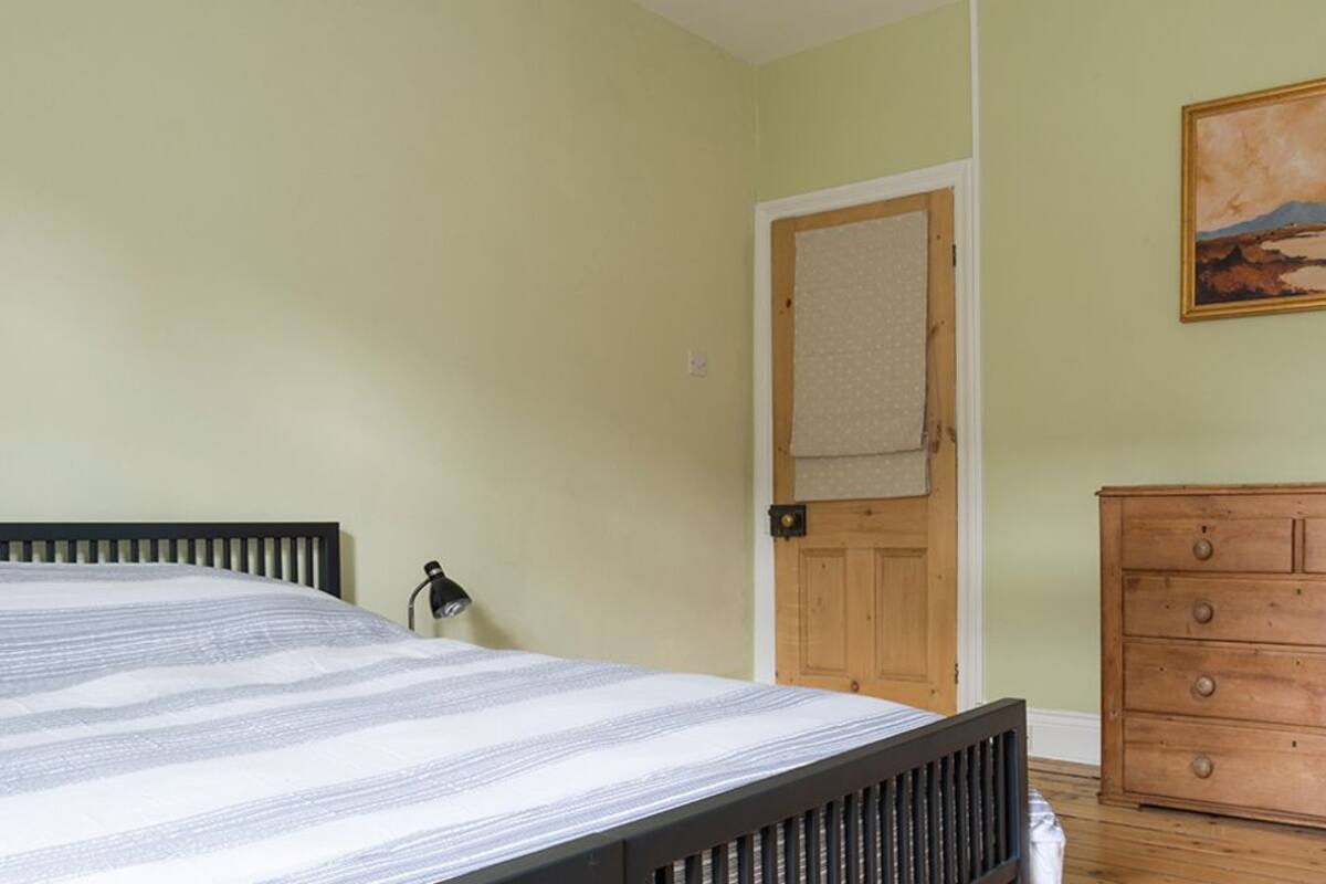 A bedroom with a bed, a wooden dresser, a door with a towel hanging, and a painting on the wall.