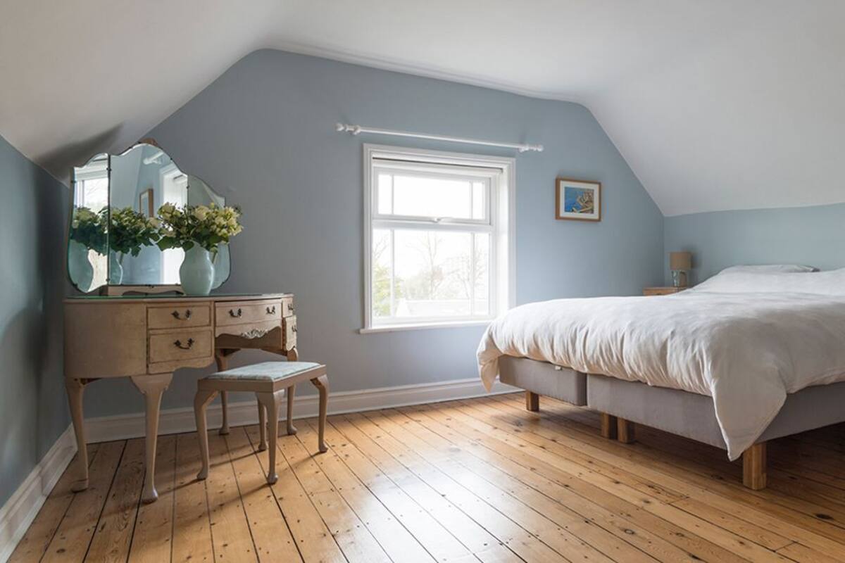 A bedroom with a sloped ceiling, a large bed, a dresser, a mirror, and a window.