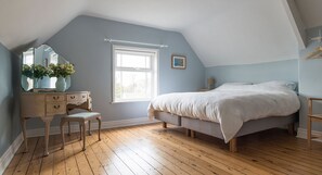 Un dormitorio con techo inclinado, una cama grande, un aparador, un espejo y una ventana.