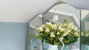A vintage-style dresser with a glass top and a white vase with flowers. - Hexham Town Bed and Breakfast (Hexham)