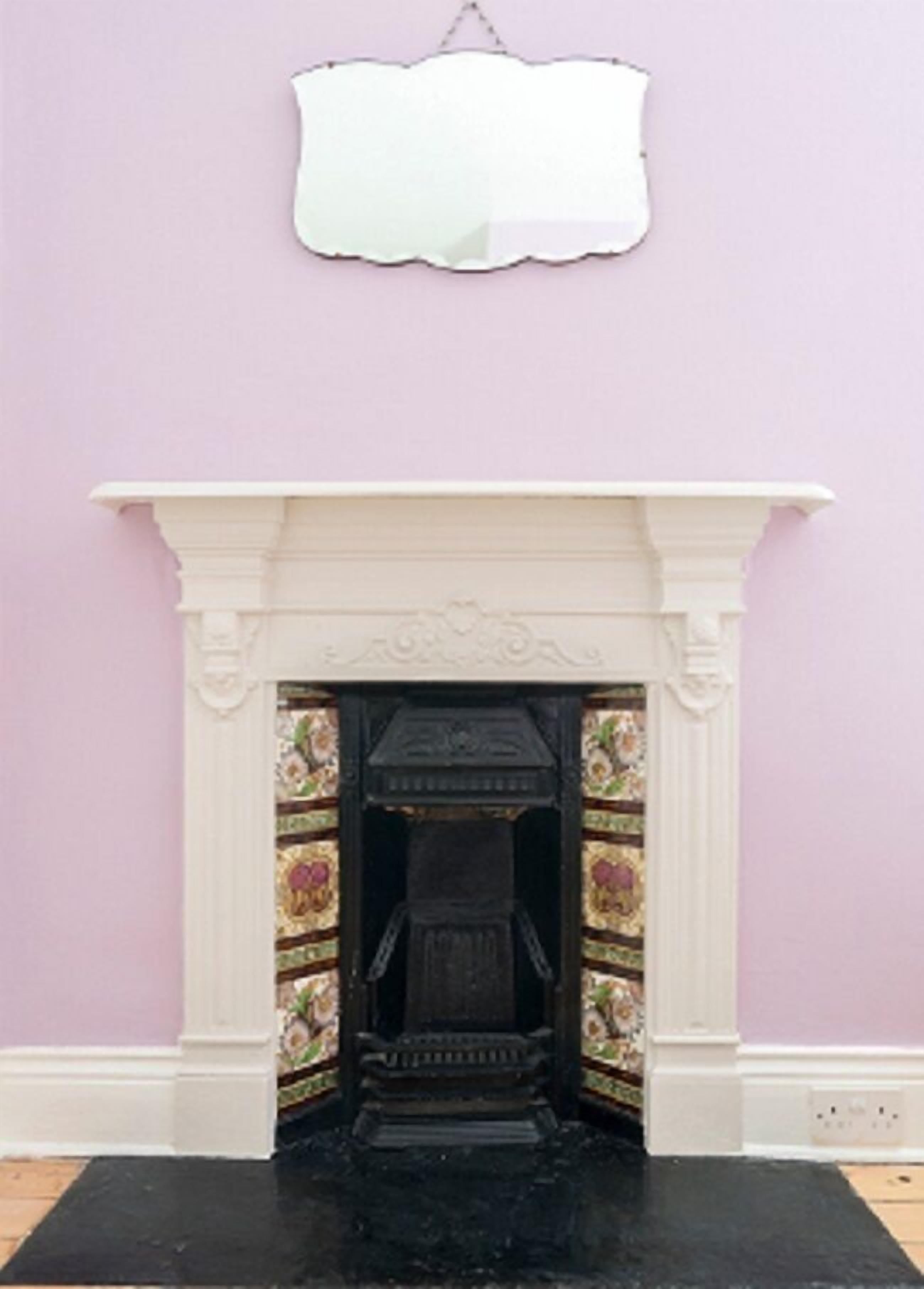 A fireplace with a white mantel and a decorative surround, set against a light purple wall.