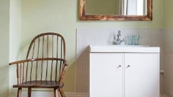 Un baño con una silla de madera, un mueble blanco y un espejo en la pared.