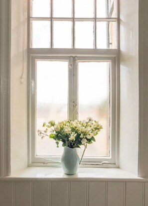 Una ventana con marco blanco y un florero con flores blancas en el alféizar.