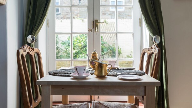 A dining table with a teapot, cups, and saucers by a window with curtains. - Hexham Town Bed and Breakfast (Hexham)