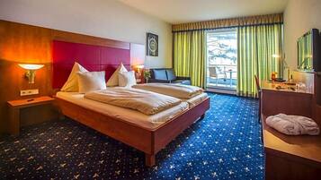 Ein Hotelzimmer mit einem großen Bett, einem Schreibtisch, einem Stuhl und einem Fenster mit Vorhängen.