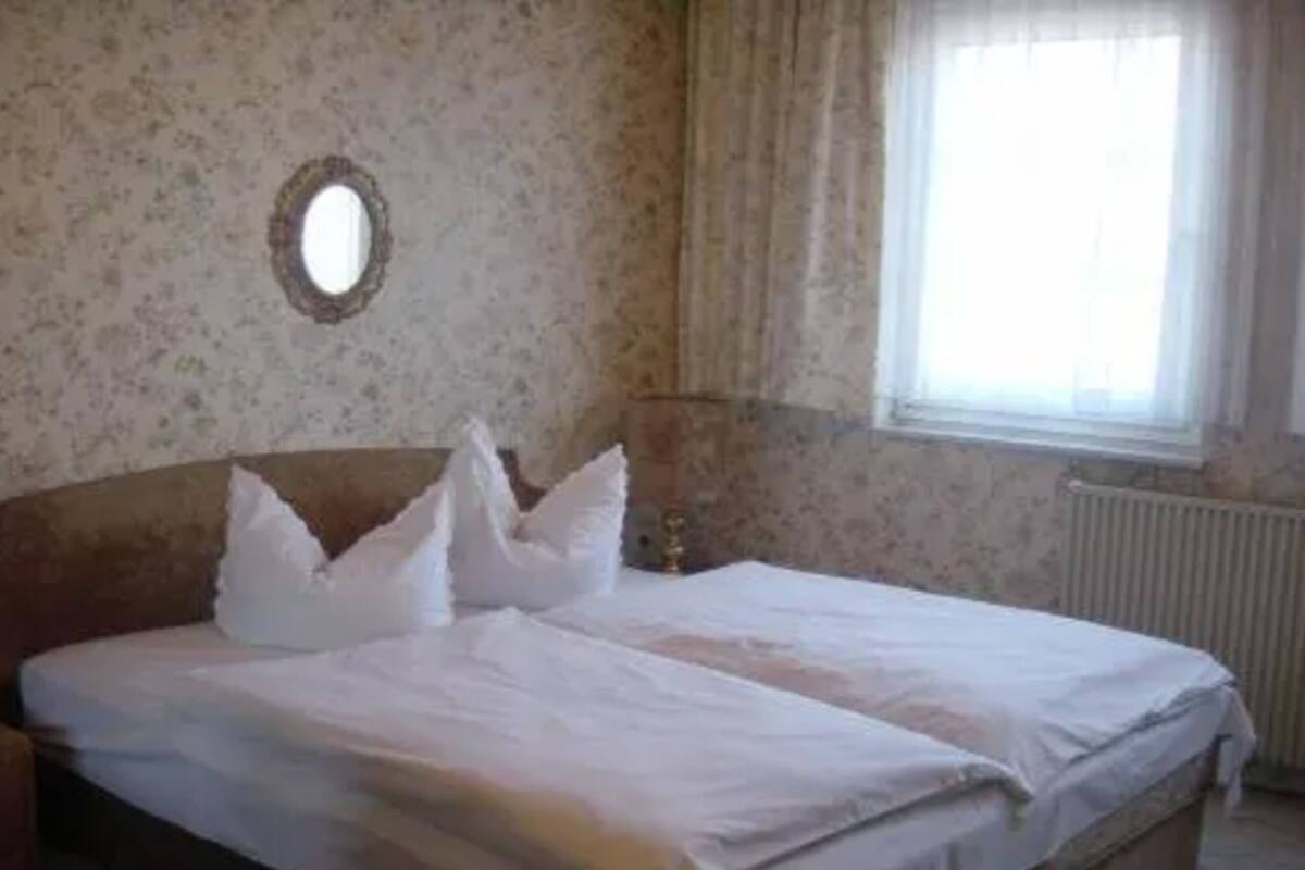 A bedroom with a bed, a round mirror on the wall, and a window with curtains.