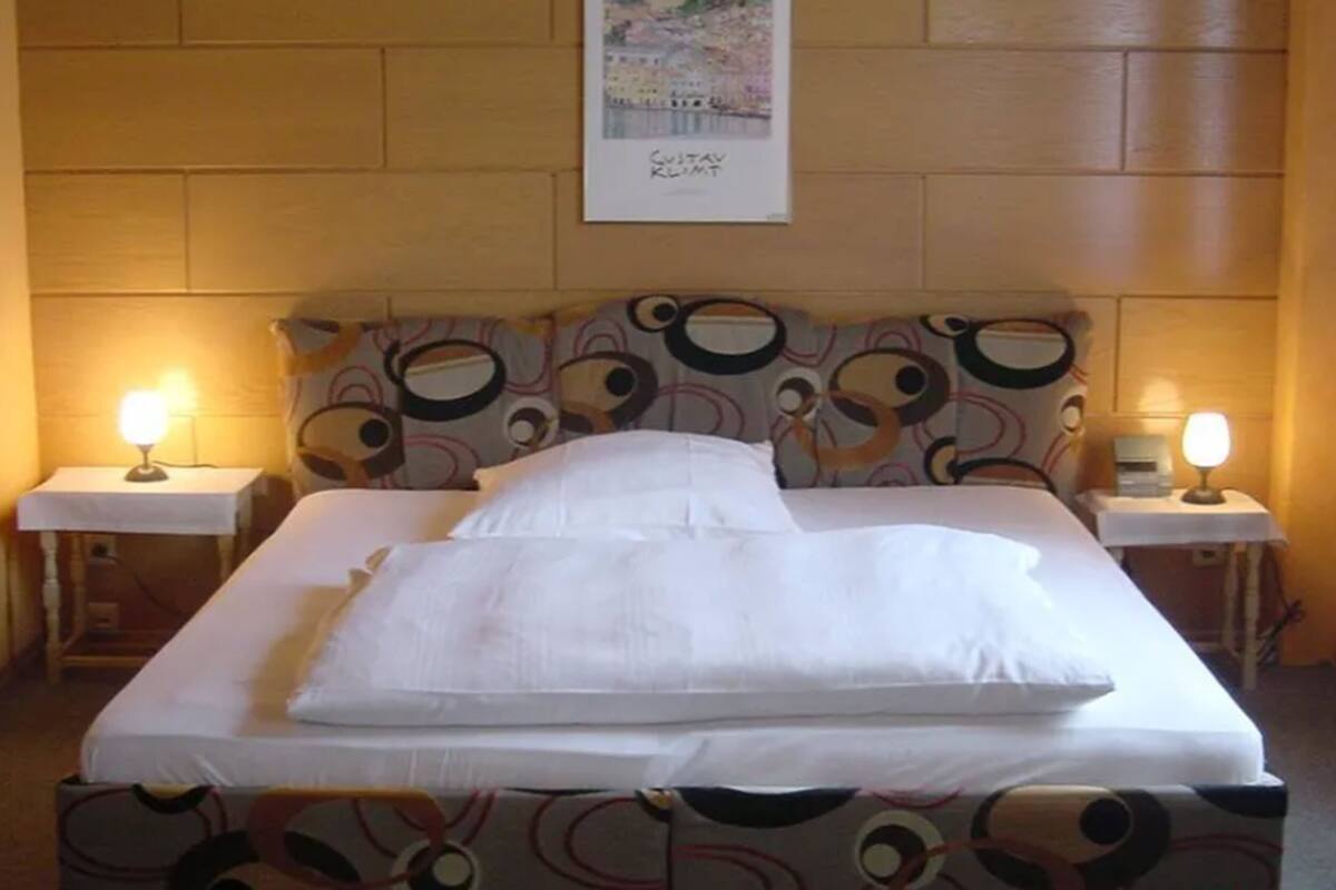 A neatly made bed with white linens in a room with a patterned headboard. There are two bedside lamps on either side of the bed.