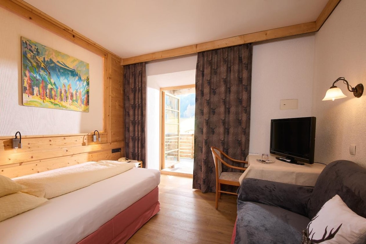 Una habitación de hotel con una cama, televisor, sofá y un cuadro en la pared.