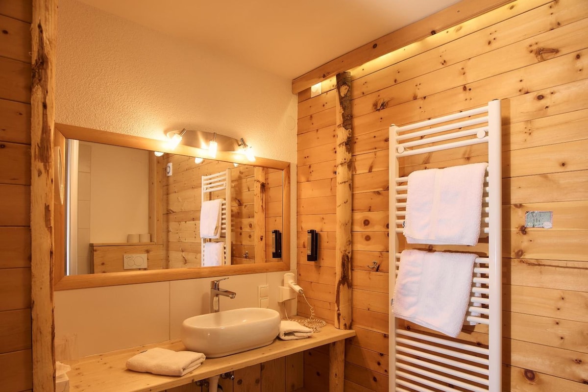 Un baño estilo cabaña de madera con un espejo grande, un lavamanos y un perchero para toallas.